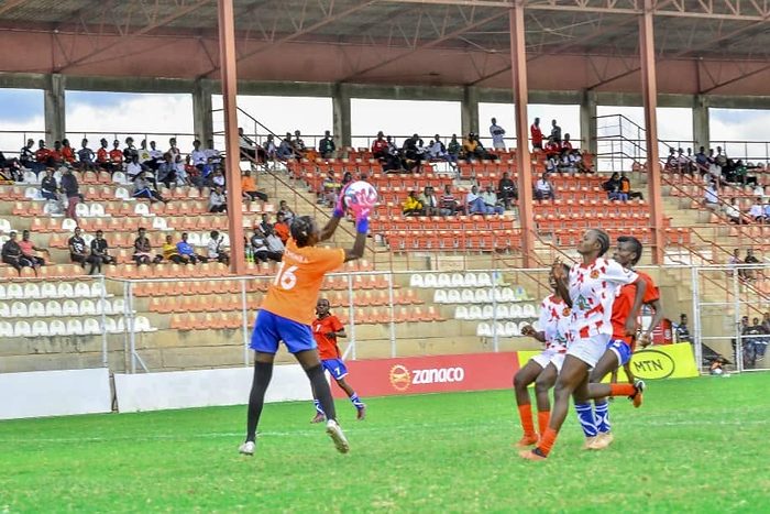 A Chipata Girls FC goalkeeper rises to claim the ball above a crowd of players, in front of a stand of watching supporters.